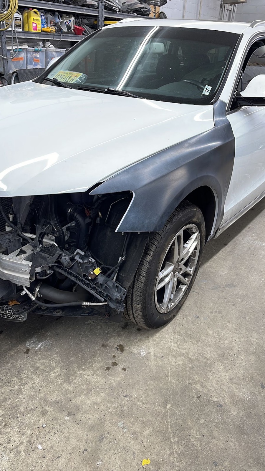 White Audi in repair with its front bumper removed and a fender in grey primer