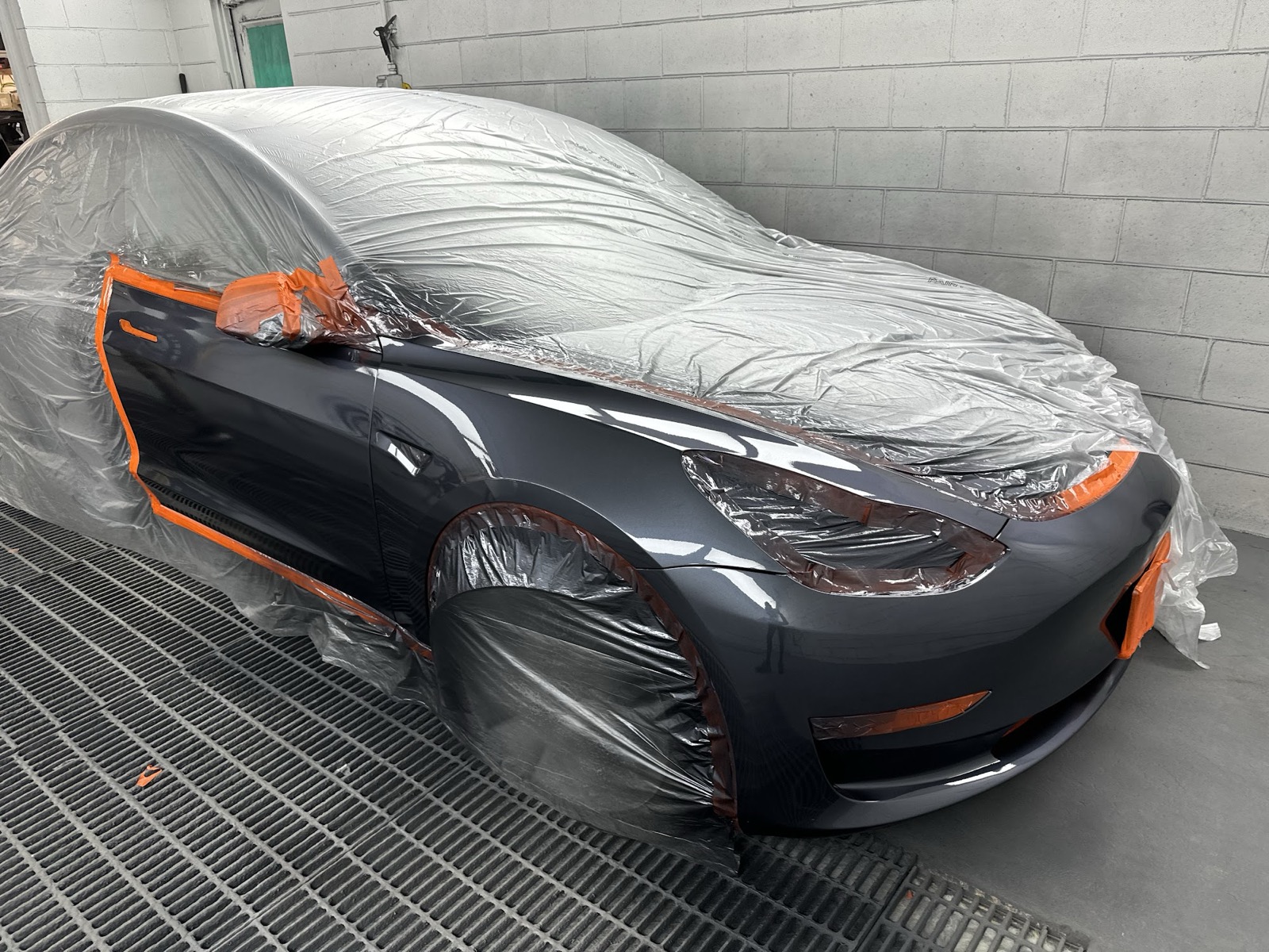 Grey Tesla masked in plastic and orange tape in the paint booth
